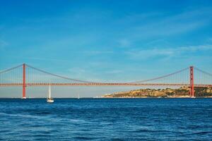 se av 25 de abril bro över tagus flod, christ de kung monument och en Yacht båt på solnedgång. Lissabon, portugal foto