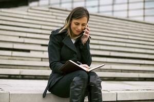 affärskvinna använder sig av telefon och personlig arrangör medan arbetssätt utomhus. foto