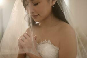 skön brud i bröllop klänning täckt förbi vit slöja, hopfällbar henne vapen och bön- på ceremoni, kärlek och äktenskap begrepp foto