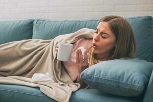 utmattad kvinna hosta och dricka te medan har feber. foto