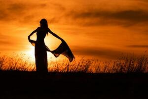 Lycklig kvinna dans och innehav scarf medan åtnjuter utgifterna tid på solnedgång. foto