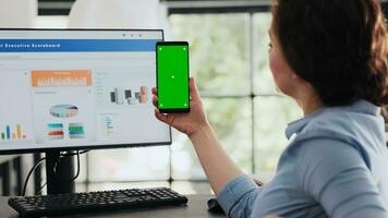 anställd innehav mobil telefon på skrivbord, ser på isolerat grönskärm layout presenteras på smartphone enhet. affärskvinna arbetssätt med modern programvara teknologi, Chromakey mockup. foto