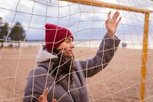 fängslande bild av kvinna i höst klädsel Framställ med fotboll mål netto på strand foto