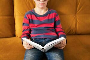 ung nyfiken pojke med glasögon fördjupning in i en bok på de soffa foto