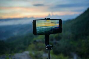 smartphone tar Foto av berg ström med stativ natur se på skärm på solnedgång