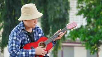 ung asiatisk pojke är spelar gitarr i en lokal- parkera, mjuk och selektiv fokus foto