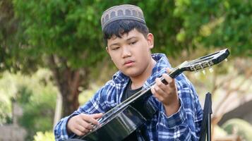 ung asiatisk pojke är spelar gitarr i en lokal- parkera, mjuk och selektiv fokus foto