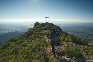 kvinna med vandring poler når de topp av en berg var där är en korsa. foto