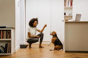 svart ung kvinna leende medan hon lekte med sin hund hemma foto