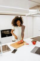 svart ung kvinna som gör frukost medan hon använder bärbar dator i köket