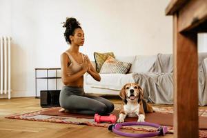 svart ung kvinna mediterar under yogapraksis med sin hund foto
