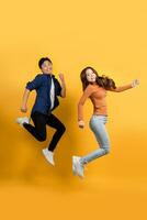 Lycklig leende asiatisk par i tillfällig kläder är Hoppar med glädje isolerat på gul studio bakgrund. foto