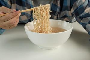 hungrig avslappnad thailändsk man använder ätpinnar för att äta varma snabbnudlar i vit kopp under lunchpauser, snabb, god och billig. traditionell hälsosam asiatisk snabbmatsmåltid av japansk och kinesisk livsstil. foto