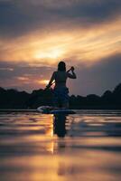 flicka på paddla styrelse i solnedgång foto