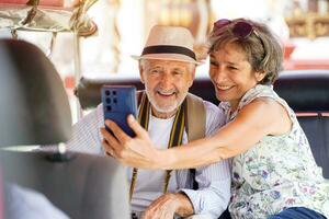 närbild amerikan senior turist man med hans vän europeisk ta en Foto selfie i en tuktuk thailand taxi på suddig av stad och Sol ljus bakgrund. senior turist begrepp