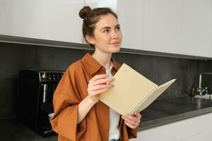 porträtt av underbar ung kvinna läsning, studerande stående i de kök med planerare, håller på med läxa, reviderar för examen foto