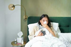 covid19, influensa och vaccination begrepp. koreanska flicka liggande i säng med kall, fångst influensa, dricka varm te och använder sig av föreskrivs medicin foto