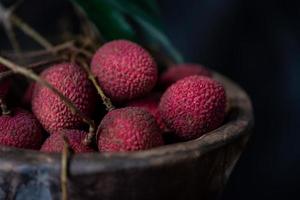 litchi läggs i en träplatta, skalad eller oöppnad, på ett mörkt träkornbord foto