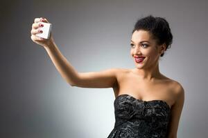 porträtt av en skön framgångsrik leende flicka håller på med selfie i svart klänning på ljus bakgrund foto