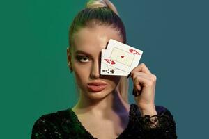 blond flicka i Smycken och svart paljett klänning. hon har täckt henne öga med två ess medan Framställ mot färgrik bakgrund. poker, kasino. närbild foto