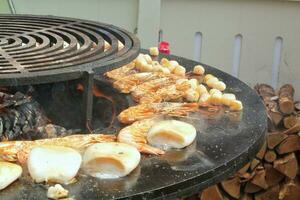 skaldjur skivor är kokta på en brand grop yta i de form av kon formad skål. skålformad platt grill med bläckfisk och räka. utomhus- utegrill matlagning. gata mat begrepp. rostat bröd de varm grillad foto