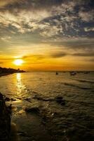 skön solnedgång med silhuetter av människor och fiske båtar på de strand foto