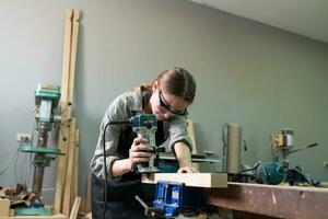 en ung kvinna snickare arbetssätt projekt i henne verkstad. kvinna snickare framställning trä- möbel. foto