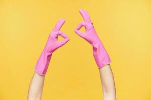 två händer i sudd handskar uttrycker positiv känslor och formning väl Gjort gest med Uppfostrad fingrar, isolerat över orange bakgrund. mänsklig händer och gestikulerar begrepp foto
