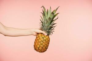 sida se av Söt kvinnas hand med naken manikyr klämma fingrar medan innehav stor färsk ananas, varelse isolerat mot rosa bakgrund foto