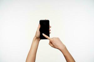 horisontell Foto av ung kvinnas händer varelse Uppfostrad medan förvaring mobil telefon och svep med pekfinger på skärm, Framställ över vit bakgrund