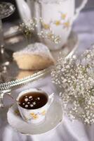 vit fortfarande liv med cheesecake och Gypsophila och kopp av te, ljus och luftig foto