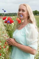 skön medelålders blond kvinna står bland en blommande fält av vallmo foto
