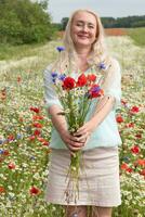 skön medelålders blond kvinna står bland en blommande fält av vallmo foto