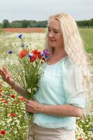 skön medelålders blond kvinna står bland en blommande fält av vallmo foto