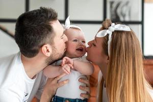 ganska yong familj i lägenhet. föräldrar kysser sin bebis foto