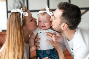 en mamma och pappa förälder kysser sin unga bebis foto