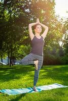 ung kvinna håller på med yoga övningar i de sommar stad parkera. foto