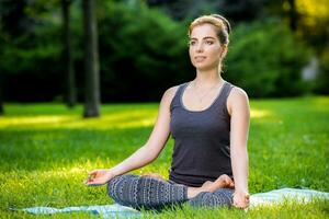 ung kvinna håller på med yoga övningar i de sommar stad parkera. foto