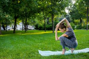 ung kvinna håller på med yoga övningar i de sommar stad parkera. foto