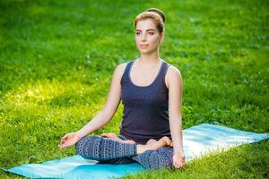 ung kvinna håller på med yoga övningar i de sommar stad parkera. foto