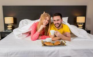 Lycklig ung par har frukost bricka på säng på Hem foto