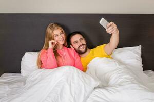 ung Lycklig par på säng håller på med selfie med telefon kamera. foto