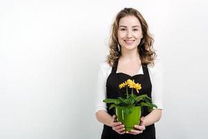 vacker, leende flicka håller en blomkruka i sina händer, poserar i studion på en vit väggbakgrund foto