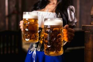 ung sexig oktoberfest servitris, bär en traditionell bavarian klänning, tjänande stor öl muggar på bar. foto
