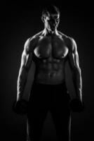 muskulös man som visar perfekt kropp med hantlar på svart backgr foto