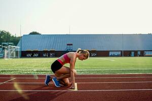 ung kvinna idrottare på startande placera redo till Start en lopp på racerbana. foto
