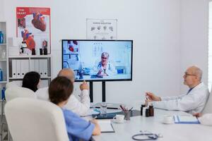 sjukhus lagarbete diskuterar med neurolog senior läkare under uppkopplad videosamtal telefonkonferens diskuterar sjukdom symptom förklara piller behandling. neurologer team arbetssätt i möte rum foto