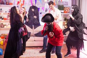 läskigt man klädd upp tycka om en pirat håller på med karaoke på halloween fest för hans vänner. foto