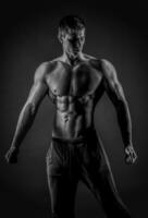 sexig muskulös man Framställ med naken torso på svart bakgrund foto