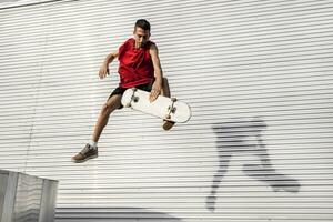 ung skateboarder hoppar upp med hans styrelse i främre av en metall bakgrund foto